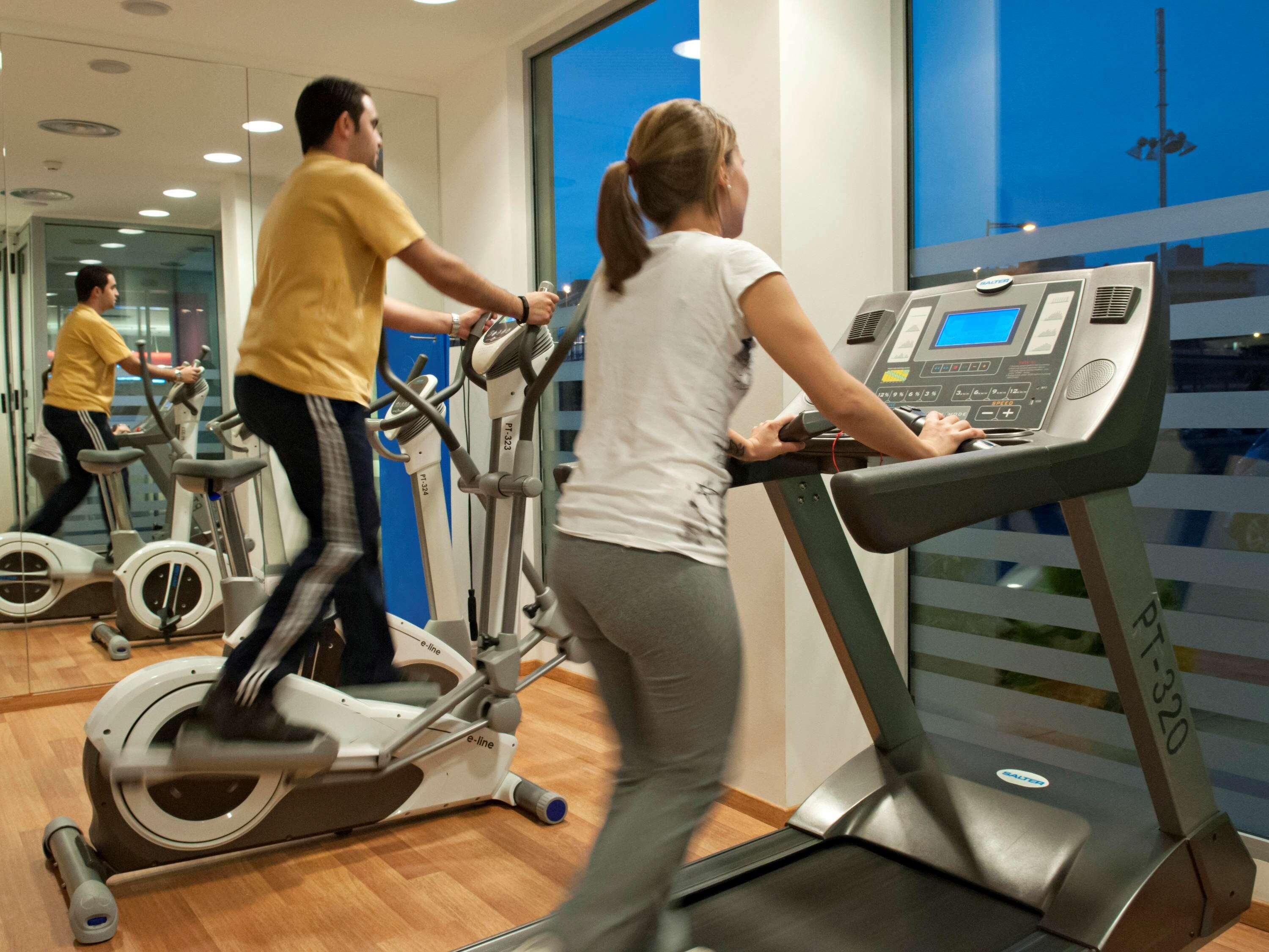 Un gimnasio con bicicletas estáticas, cintas de correr y un espejo grande.
