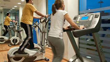 Un gimnasio con bicicletas estáticas, cintas de correr y un espejo grande.