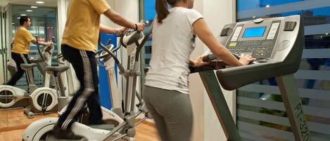 Un gimnasio con bicicletas estáticas, cintas de correr y un espejo grande.
