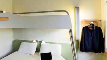 Una cama litera con un ordenador portátil en la cama inferior, un perchero y una mesita de noche con una lámpara.