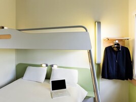 Una cama litera con un ordenador portátil en la cama inferior, un perchero y una mesita de noche con una lámpara.