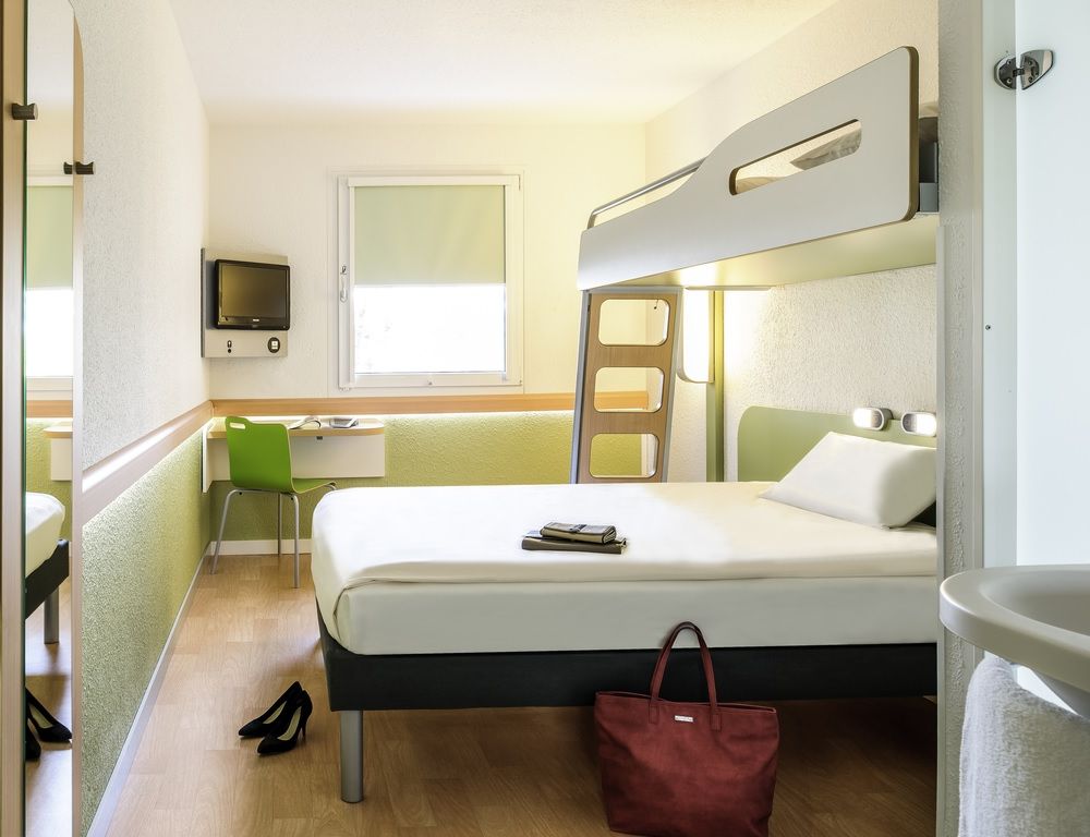 Habitación de hotel compacta con literas, un escritorio con silla, televisor y ventana.