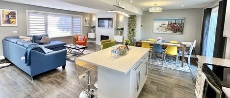A modern living room with a blue sofa, a dining area with yellow chairs, and a kitchen with a central island.