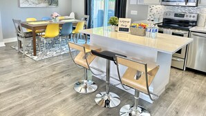 A modern kitchen with a central island, stainless steel appliances, and a dining area with yellow chairs. - Fall Special: Stay Longer & Save Up to 40% in Niagara! (St. Catharines)