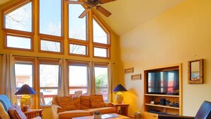 Un ampio soggiorno con ampie finestre, una ventola a soffitto, una televisione e un camino.