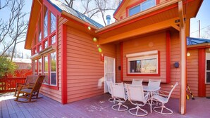 Una casa a due piani con facciata rossa e un patio in legno. Sul patio ci sono sedie bianche e una poltrona a dondolo.