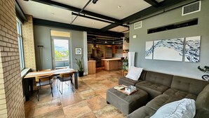 Une cuisine moderne avec des meubles en bois et un grand îlot central, un coin repas avec une table et des chaises en bois, et un salon avec un canapé et une table basse.