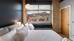 Une chambre avec un grand lit, une fenêtre donnant sur une montagne et un mur en briques.