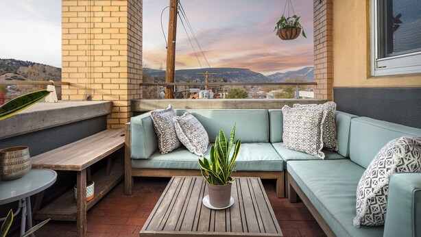 Un balcon avec un canapé bleu clair, une table en bois et une plante suspendue.