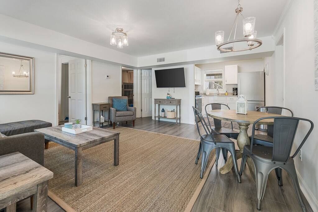 A modern living room with a dining area, a kitchen, and a TV mounted on the wall.