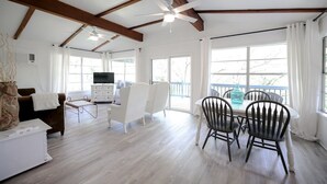 Un salón amplio con techo de madera, un comedor con sillas, un televisor y un ventanal grande con cortinas.