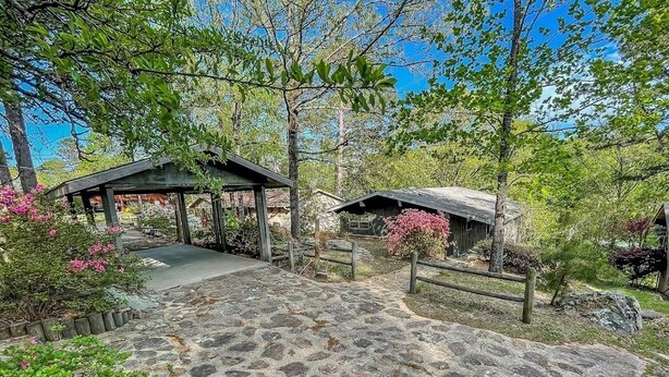 Un sendero de piedra conduce a una estructura rústica de madera con un porche cubierto, rodeada de exuberante follaje y plantas florecientes.