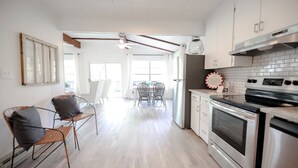 Una cocina moderna con electrodomésticos de acero inoxidable, un comedor con mesa y sillas blancas, y un amplio ventanal que proporciona luz natural.