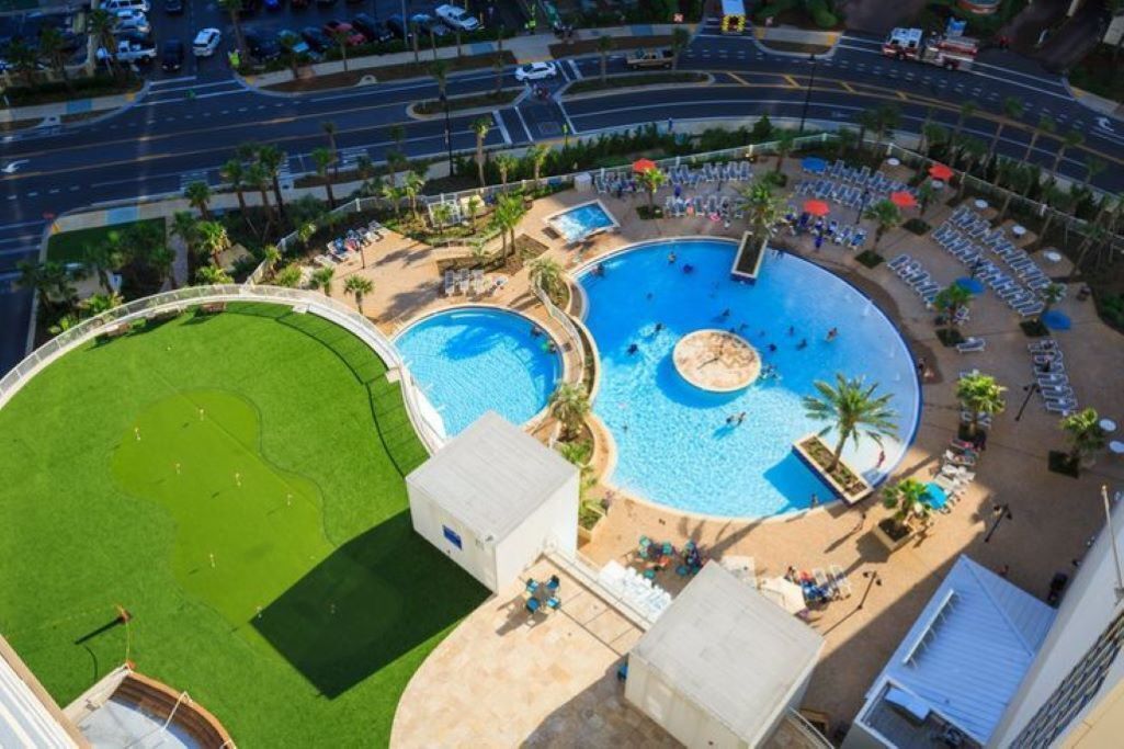 Amplia zona de piscina al aire libre con varias piscinas, rodeada de sillas de descanso y palmeras.
