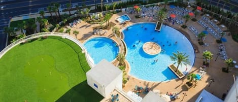 Amplia zona de piscina al aire libre con varias piscinas, rodeada de sillas de descanso y palmeras.
