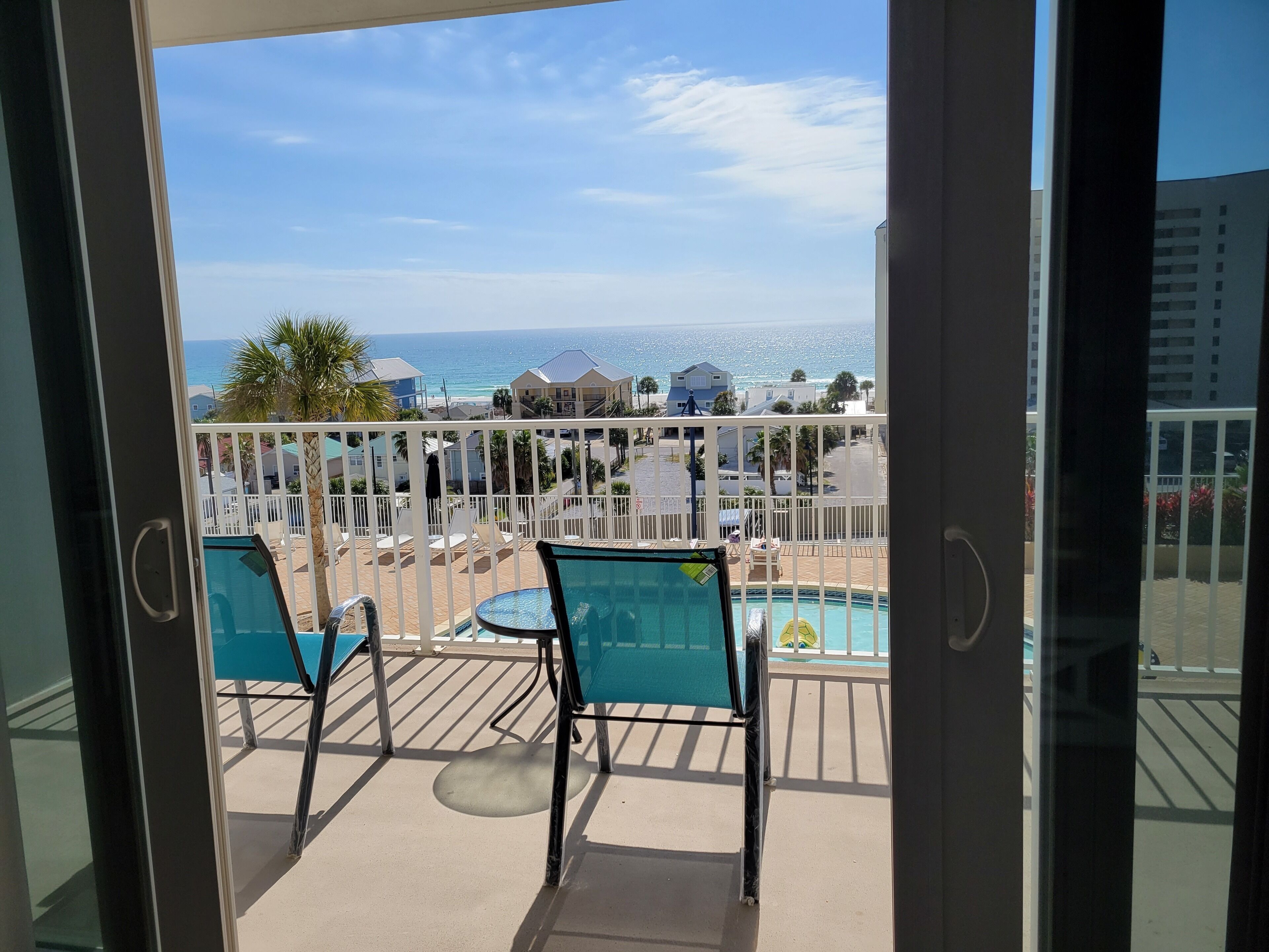 Ein Balkon mit Blick auf das Meer und den Strand, ausgestattet mit zwei Stühlen und einem kleinen Tisch.
