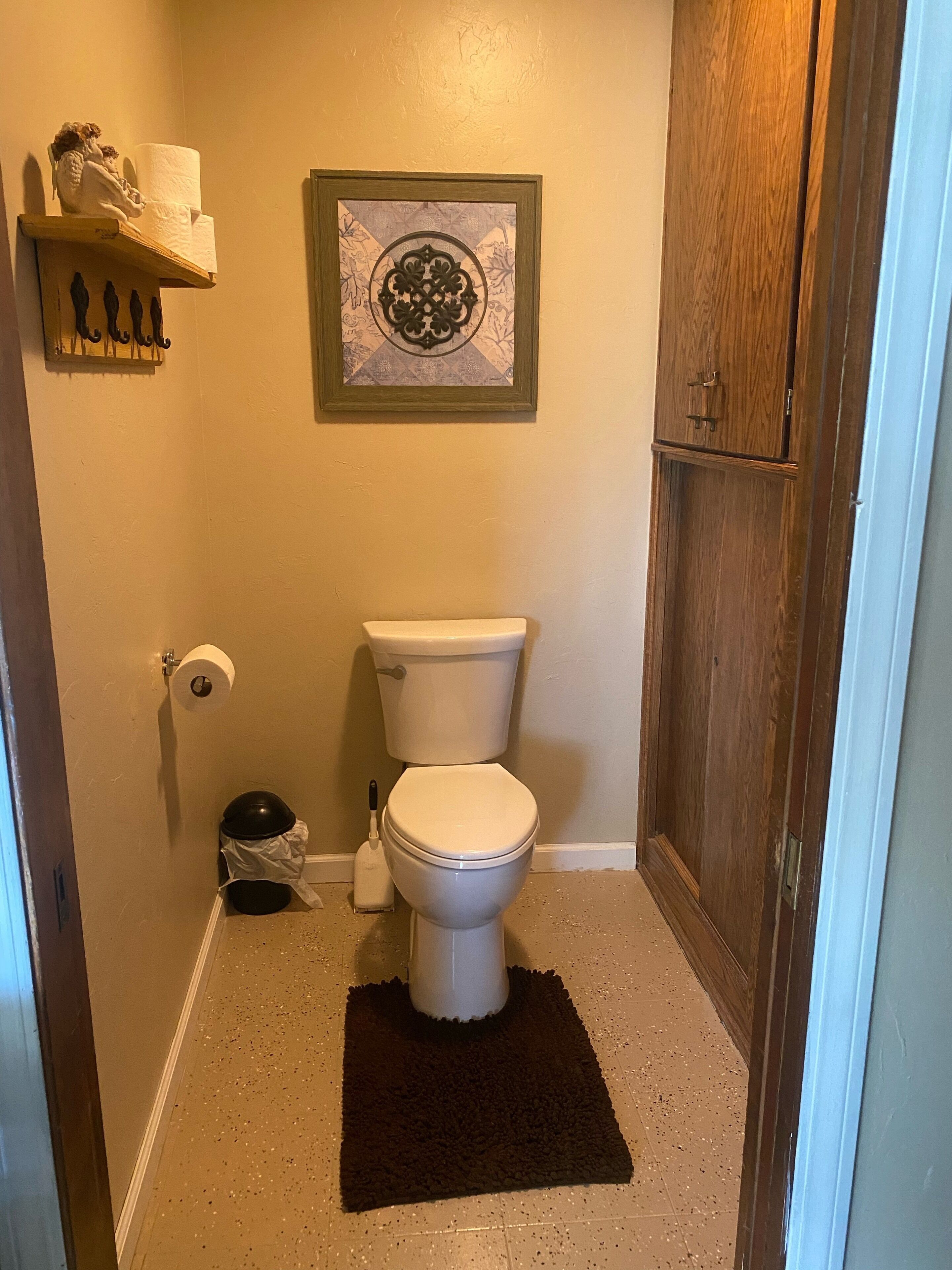 Ein kleines Badezimmer mit Toilette, Toilettenpapierhalter, Mülleimer und einer dekorativen Wanddekoration.