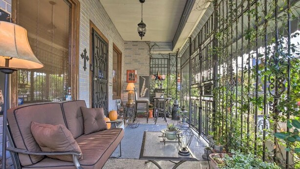 A covered outdoor patio with a sofa, table, and potted plants. - La Villa By The Rivewalk Gardens & Pavilions (San Antonio)