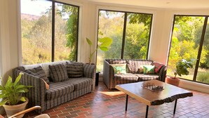 A spacious room with a large window, a plaid sofa, a wooden coffee table, and a brick floor.