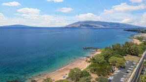 Une vue côtière avec une plage, une mer bleue et limpide, et une montagne à l’horizon.