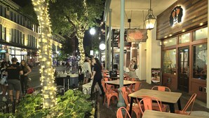Un espacio al aire libre para comer con mesas y sillas, luces colgantes y un restaurante con un letrero.