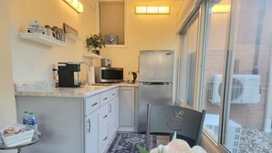Cocina compacta con refrigerador, microondas y cafetera. Hay una pequeña mesa con una escultura de caballito de mar, y una ventana con unidad de aire acondicionado en el exterior.