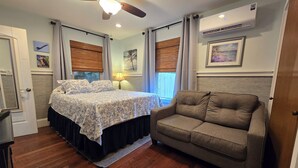 Een slaapkamer met een bed, een slaapbank, een plafondventilator, een raam met zonwering en een airconditioning.