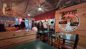 Een restaurantinterieur met houten zithoeken, groene tafels en een bord met pizzaschilderingen.