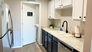 A kitchen with white cabinets, a granite countertop, a dishwasher, and a sign on the door that says "Alexa, do the laundry." - Newly remodeled condo minutes to the Strip, Lake & SDC with AMAZING views! (Branson)