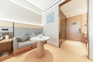 Una habitación de hotel moderna con sofá, una mesa redonda y un vidrio que da al baño.