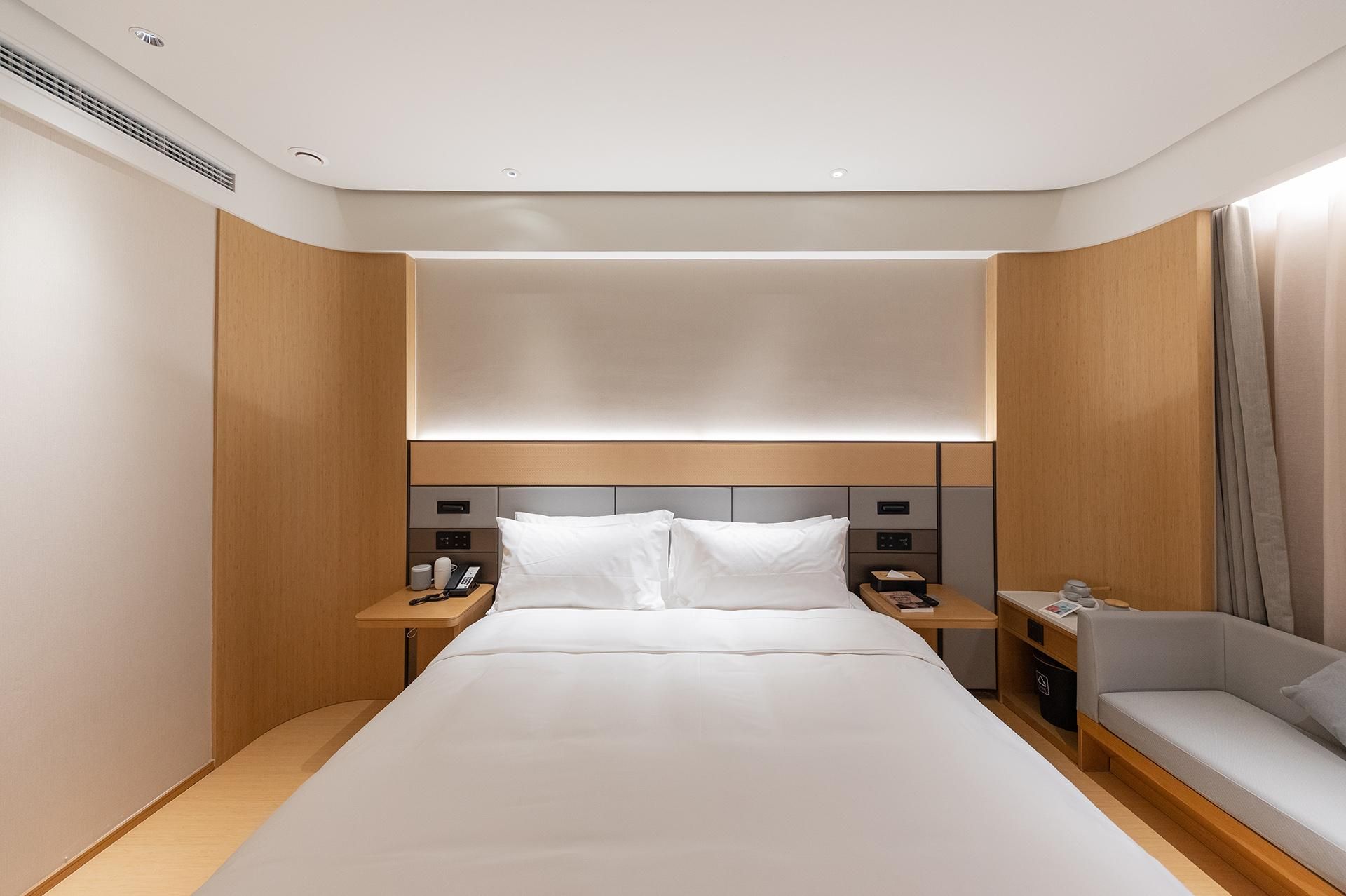 Una camera d'albergo con un letto grande, comodini, un divano e una testiera con illuminazione integrata.