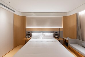 Une chambre d’hôtel avec un grand lit, des tables de chevet, un canapé et une tête de lit dotée d’un éclairage intégré.