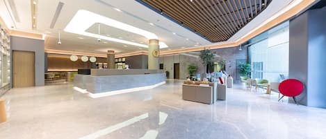 A modern lobby with a reception desk, seating area, and large windows.