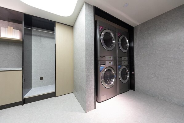 A modern laundry room with four stacked washing machines, a glass partition, and a beige cabinet.