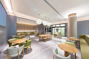 Un interior de restaurante moderno con mesas redondas, sillas verdes y una gran columna.