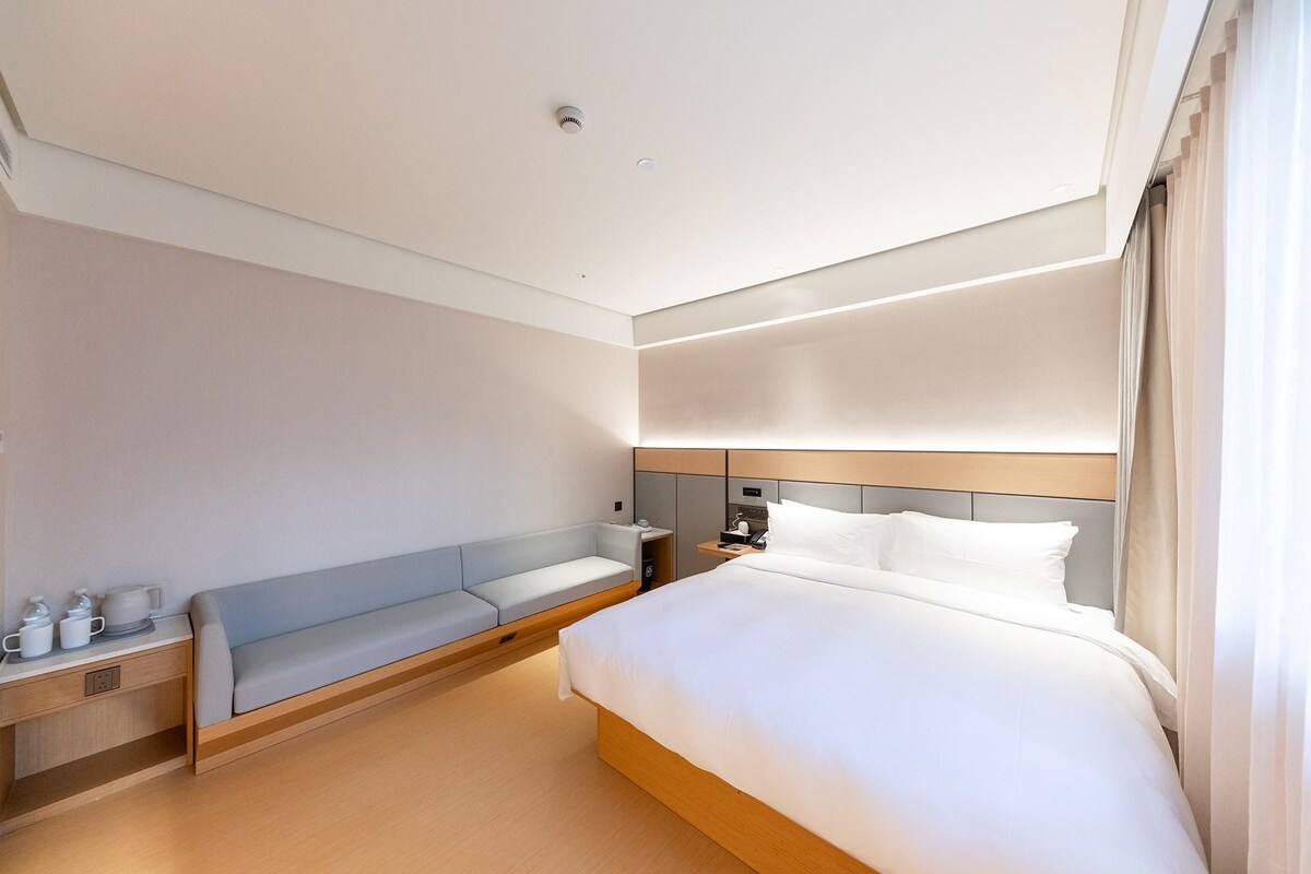 Ein modernes Hotelzimmer mit Bett, Nachttisch, Lampe und einer eingebauten Sitzbank.