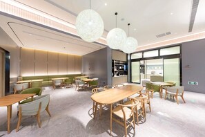A modern dining area with wooden tables and chairs, a green sofa, and pendant lighting.