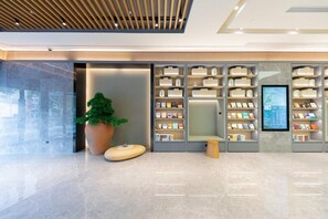 A modern reception area with a large potted plant, a seating area, and a digital display.
