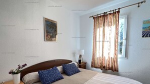 Ein Schlafzimmer mit einem Bett, einem Nachttisch, einer Lampe, einem Fenster mit Vorhängen und einem Wandbild.