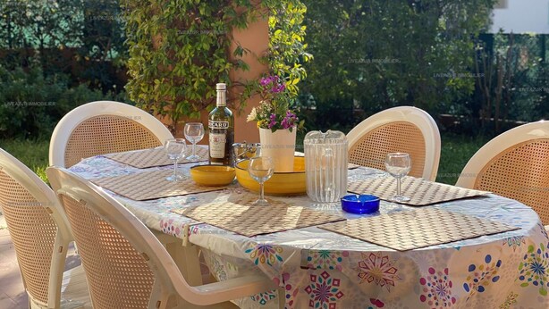 Ein Essbereich im Freien mit Korbstühlen und einem Tisch, der mit einer Flasche, Gläsern und einer Blumenvase gedeckt ist.