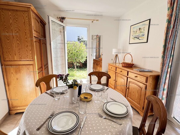 A dining area with a round table set for four, wooden cabinets, and a view of greenery outside.