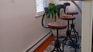 A corner room with a window, a wall clock, and three bar stools. - Home away from home (Elmont)