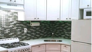 A kitchen with white cabinets, a gas stove, a microwave, and a sink. - Home away from home (Elmont)