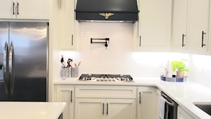 Een moderne keuken met witte kasten, een roestvrijstalen koelkast, een zwarte afzuigkap en een gasfornuis.