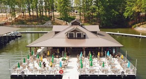 A docked boat with outdoor seating and umbrellas, surrounded by trees and a body of water.