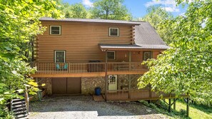 A two-story log cabin with a balcony, a stone foundation, and a gravel driveway. - Beautiful mountain view! SAUNA, HOT TUB, Pool Table, and Fast WIFI! Pet friendly (Waynesville)