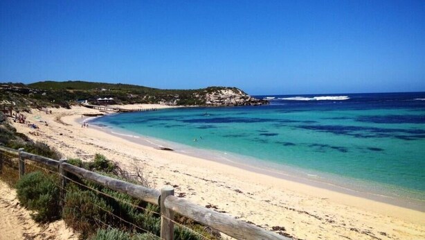A beach with clear turquoise waters, a sandy shore, and a wooden fence.