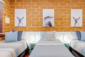 Habitación de hotel con dos camas, una pared de ladrillo y tres láminas enmarcadas con imágenes de animales.