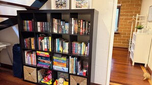 A bookshelf with various books and board games, a staircase, and a brick wall.
