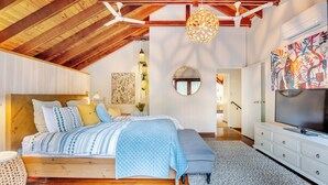 Un dormitorio con techo de madera, una cama con ropa de cama estampada, un espejo redondo y un televisor sobre un tocador.